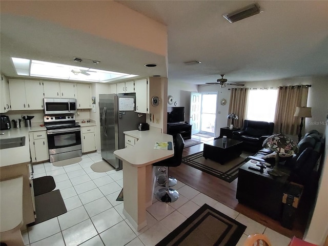 living room featuring light tile patterned floors, visible vents, ceiling fan, and a skylight