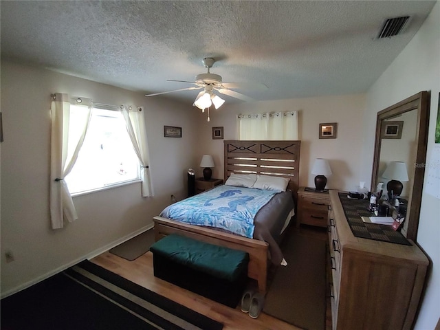 bedroom with wood finished floors, baseboards, a ceiling fan, visible vents, and a textured ceiling