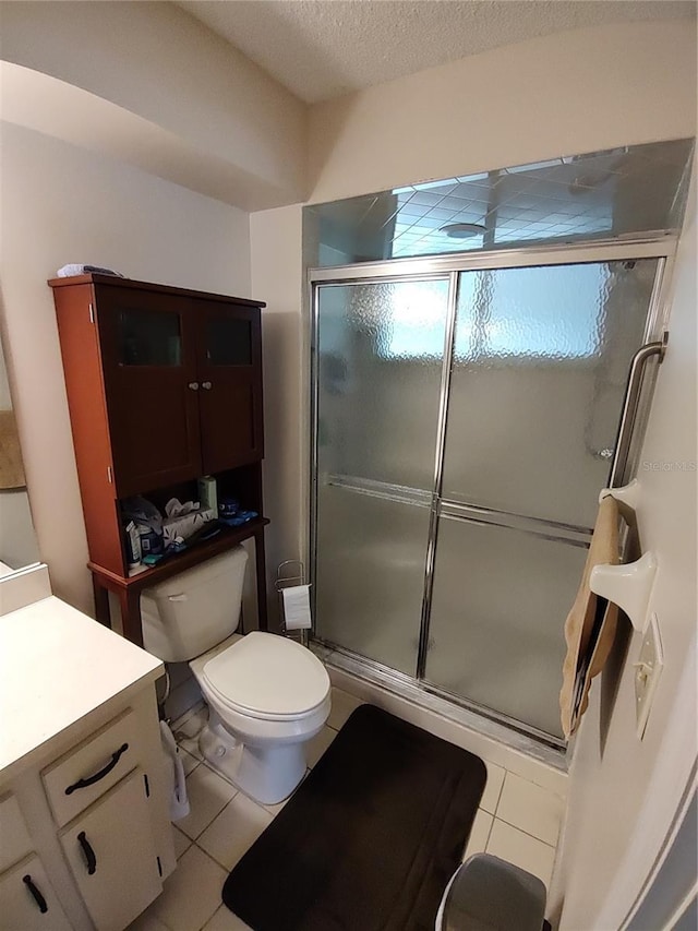 full bathroom featuring vanity, a shower stall, a textured ceiling, tile patterned floors, and toilet