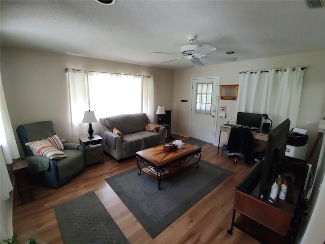 living room with a textured ceiling, ceiling fan, and wood finished floors