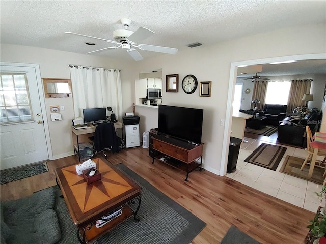 living room featuring baseboards, visible vents, ceiling fan, light wood-style floors, and a textured ceiling