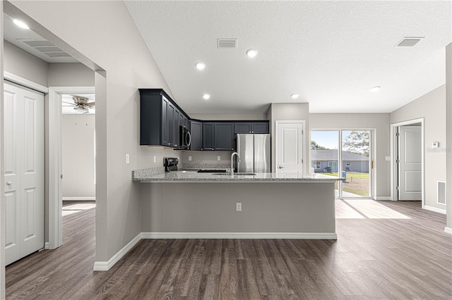 kitchen featuring lofted ceiling, sink, appliances with stainless steel finishes, light stone countertops, and kitchen peninsula