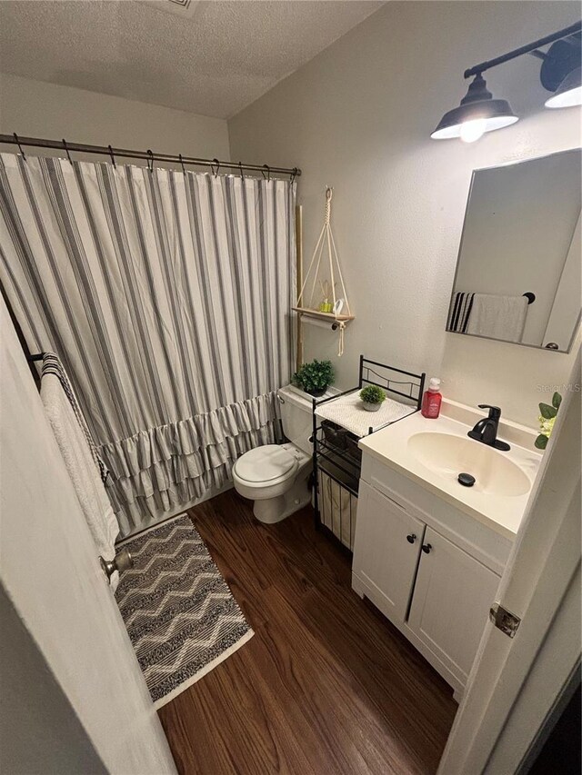 bathroom featuring a textured ceiling, vanity, wood-type flooring, walk in shower, and toilet