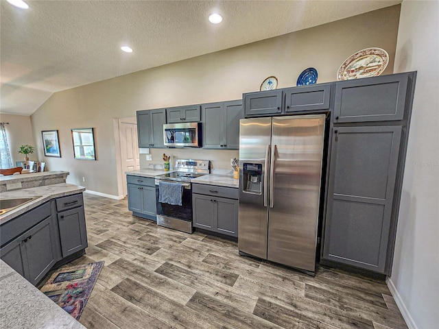 kitchen featuring appliances with stainless steel finishes, hardwood / wood-style flooring, gray cabinets, and lofted ceiling