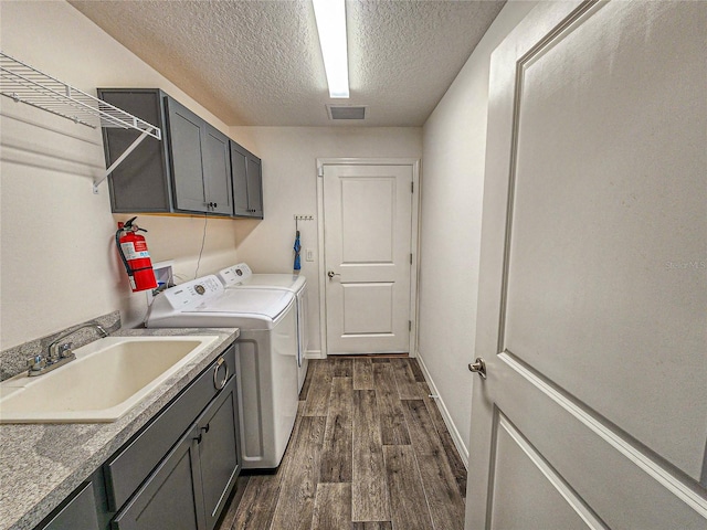 clothes washing area featuring cabinets, a textured ceiling, sink, washing machine and clothes dryer, and dark hardwood / wood-style floors