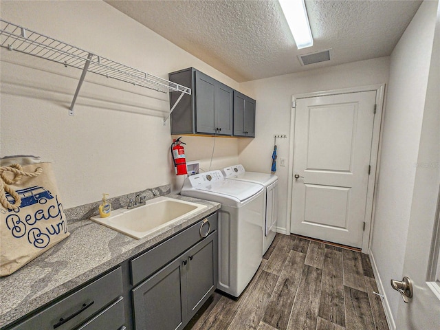 laundry room featuring washing machine and clothes dryer, sink, cabinets, dark wood-type flooring, and a textured ceiling