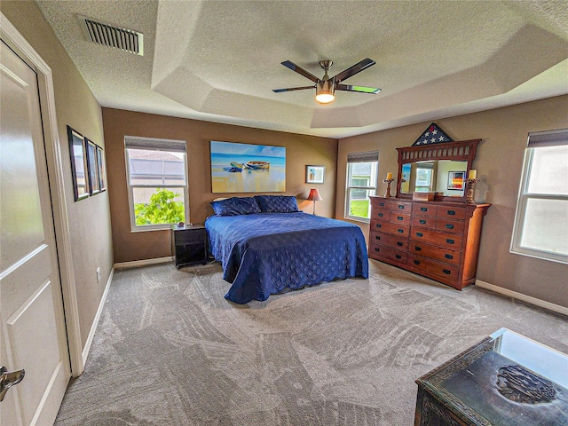 carpeted bedroom featuring ceiling fan, a raised ceiling, a textured ceiling, and multiple windows