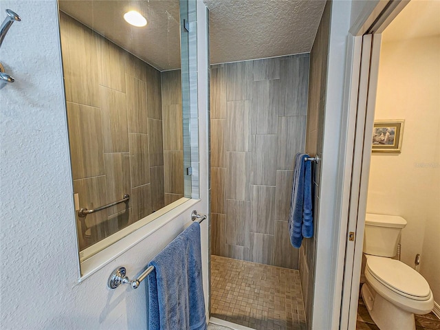 bathroom featuring tiled shower, tile patterned floors, a textured ceiling, and toilet