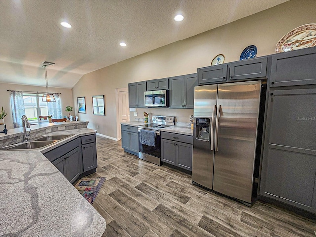 kitchen with sink, vaulted ceiling, appliances with stainless steel finishes, decorative light fixtures, and dark hardwood / wood-style flooring