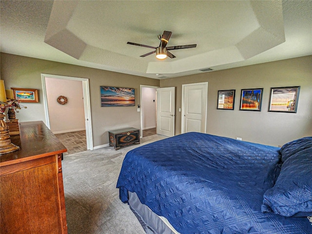 carpeted bedroom with ceiling fan, a textured ceiling, and a tray ceiling