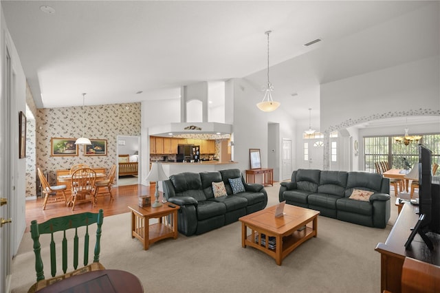 living room with high vaulted ceiling, an inviting chandelier, and light hardwood / wood-style flooring