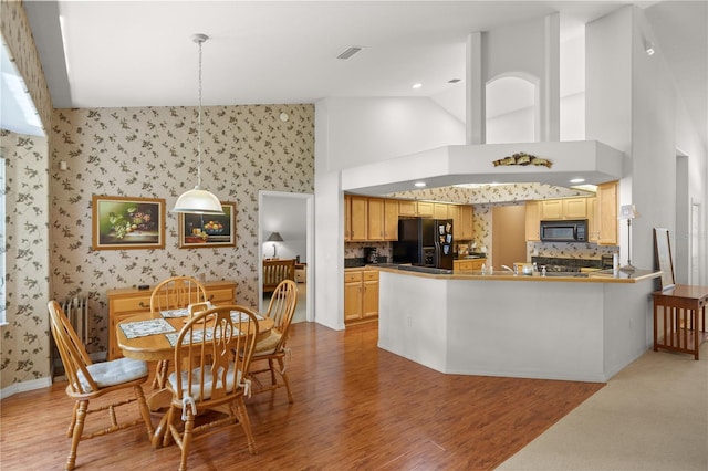 kitchen with high vaulted ceiling, light hardwood / wood-style flooring, black appliances, kitchen peninsula, and decorative backsplash