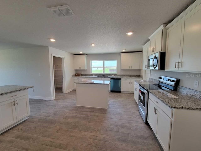 kitchen with visible vents, a kitchen island, wood finished floors, stainless steel appliances, and a sink