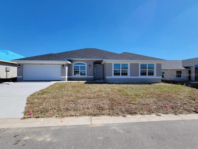 ranch-style house featuring a garage, a shingled roof, driveway, stucco siding, and a front yard