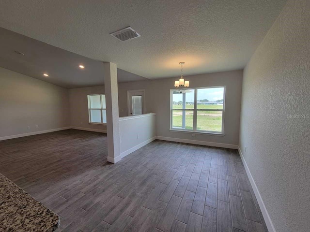 spare room with visible vents, a chandelier, dark wood-style flooring, and a textured wall