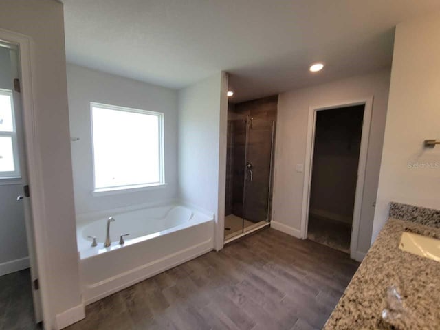 bathroom with a stall shower, wood finished floors, baseboards, a bath, and vanity