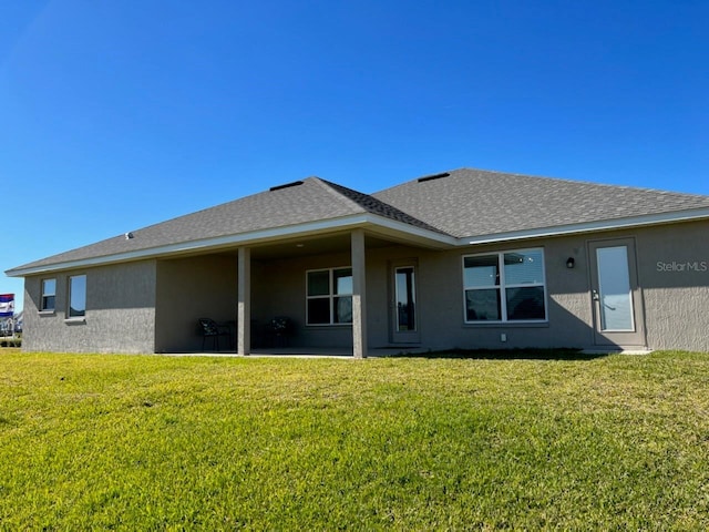 back of house with a yard, roof with shingles, and stucco siding