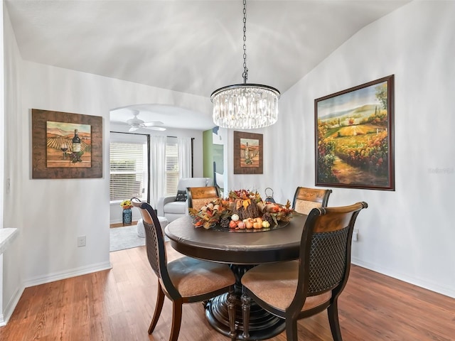 dining space featuring ceiling fan with notable chandelier, wood-type flooring, and lofted ceiling