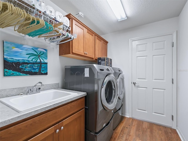 clothes washing area with light hardwood / wood-style floors, a textured ceiling, cabinets, sink, and washing machine and clothes dryer