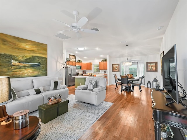 living room featuring ceiling fan with notable chandelier and light hardwood / wood-style flooring