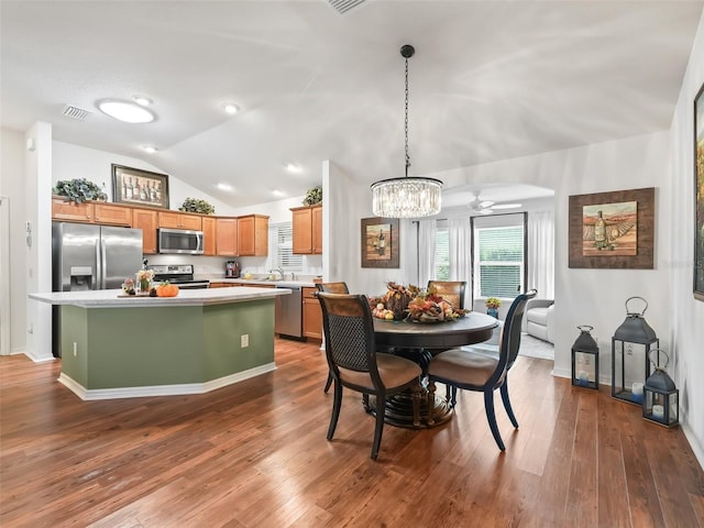 dining area featuring ceiling fan with notable chandelier, sink, dark wood-type flooring, and vaulted ceiling