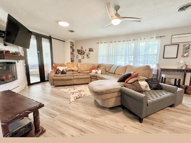 living room with a textured ceiling, ceiling fan, and light hardwood / wood-style flooring