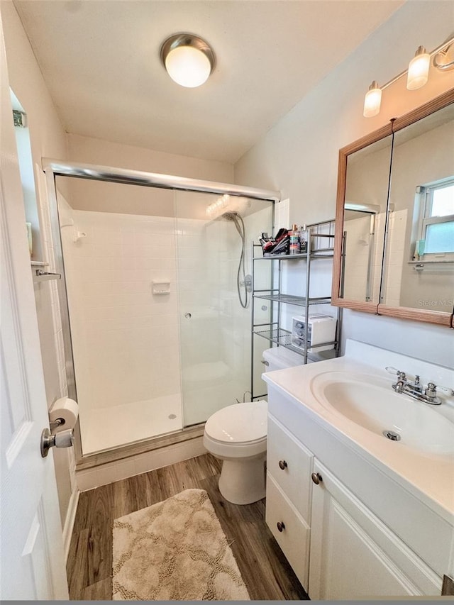 bathroom with hardwood / wood-style flooring, a shower with door, vanity, and toilet