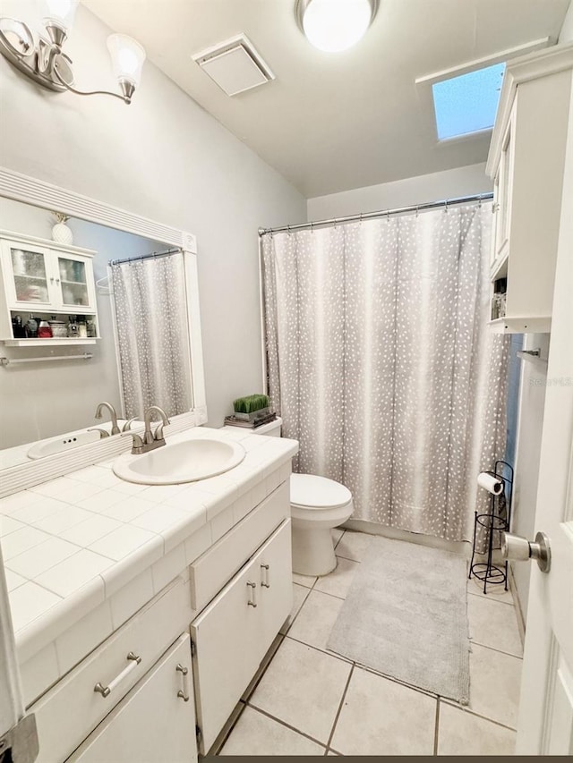 bathroom with tile patterned flooring, vanity, toilet, and a skylight