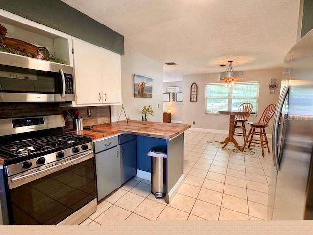 kitchen with white cabinets, hanging light fixtures, light tile patterned floors, butcher block countertops, and appliances with stainless steel finishes