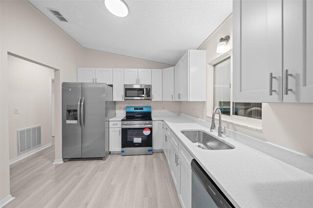 kitchen featuring light wood-type flooring, white cabinetry, vaulted ceiling, sink, and appliances with stainless steel finishes