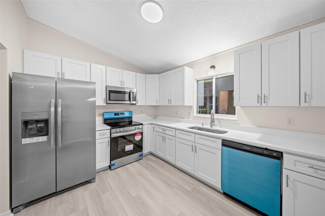 kitchen with appliances with stainless steel finishes, vaulted ceiling, sink, and white cabinets