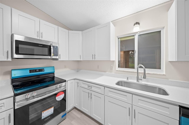 kitchen with a textured ceiling, stainless steel appliances, sink, and white cabinetry