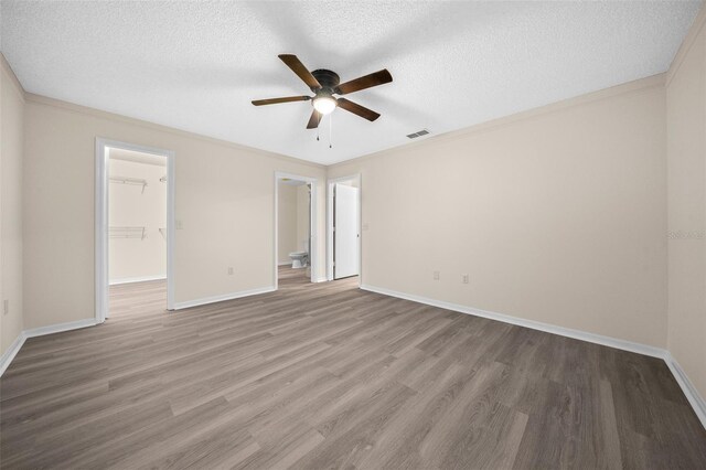 unfurnished bedroom with a textured ceiling, a spacious closet, a closet, wood-type flooring, and ceiling fan