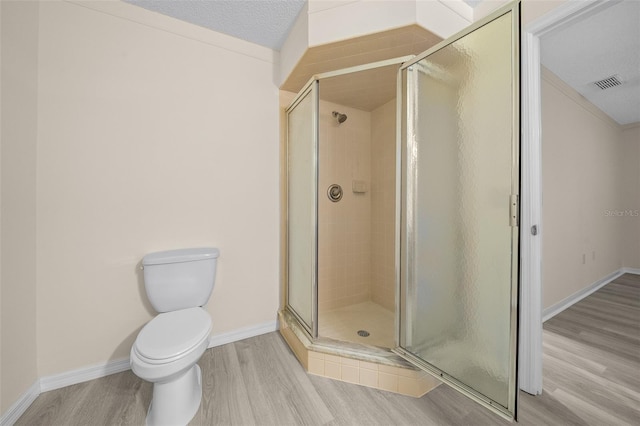 bathroom featuring toilet, hardwood / wood-style floors, an enclosed shower, and a textured ceiling