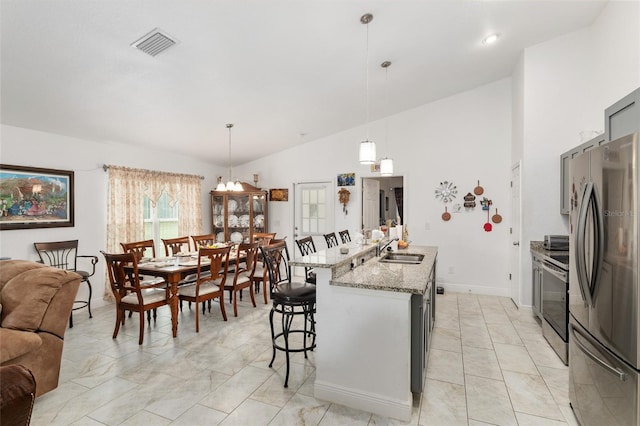 kitchen featuring decorative light fixtures, vaulted ceiling, appliances with stainless steel finishes, and a kitchen island with sink