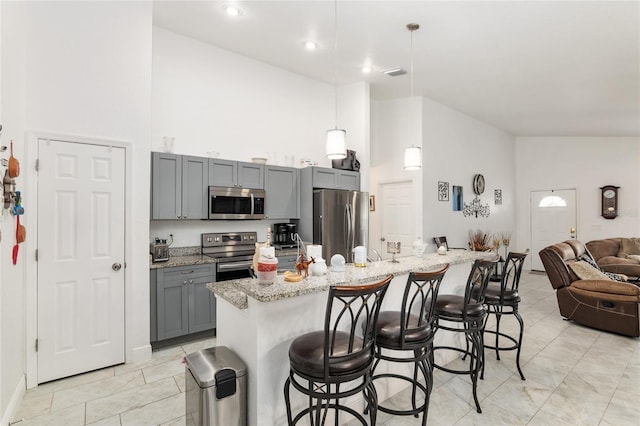 kitchen with appliances with stainless steel finishes, an island with sink, gray cabinetry, and a breakfast bar area