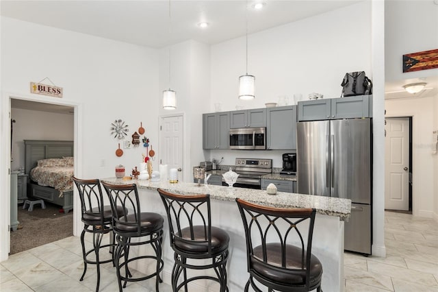 kitchen featuring gray cabinets, a breakfast bar, hanging light fixtures, light stone countertops, and appliances with stainless steel finishes