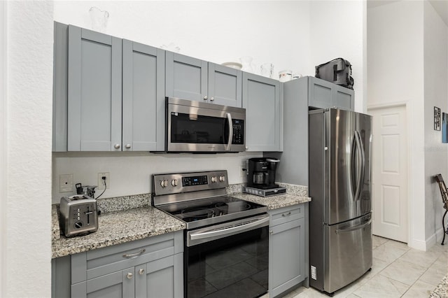 kitchen with gray cabinetry, appliances with stainless steel finishes, light tile patterned floors, and light stone counters