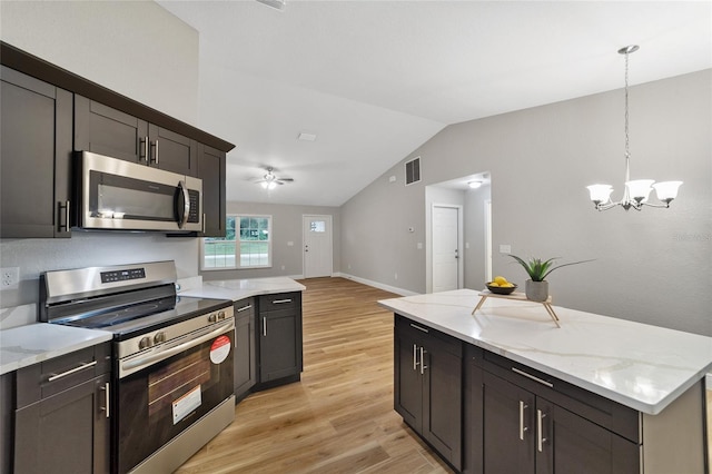 kitchen featuring light stone counters, pendant lighting, lofted ceiling, appliances with stainless steel finishes, and light wood-type flooring