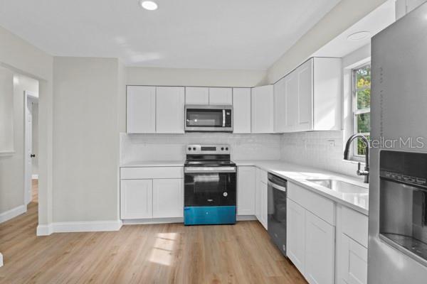 kitchen with white cabinets, backsplash, stainless steel appliances, light wood-type flooring, and sink