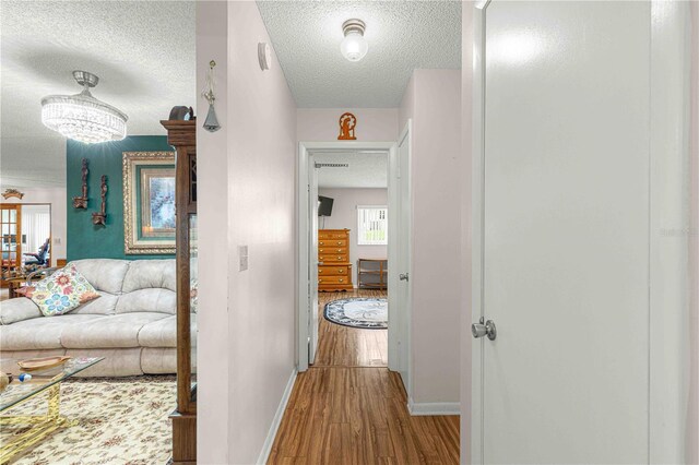 hall with hardwood / wood-style floors, an inviting chandelier, and a textured ceiling