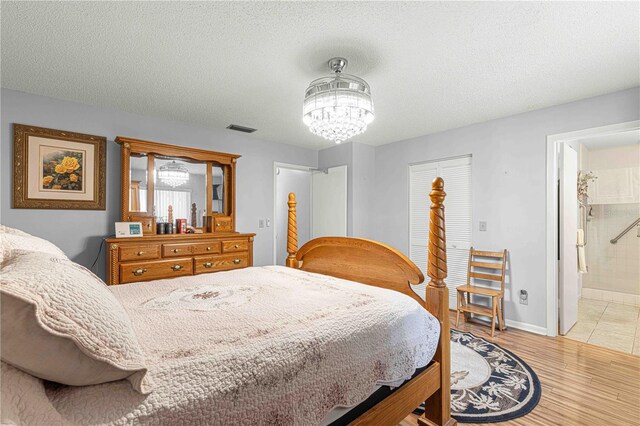 bedroom with a textured ceiling, a chandelier, light wood-type flooring, and ensuite bathroom