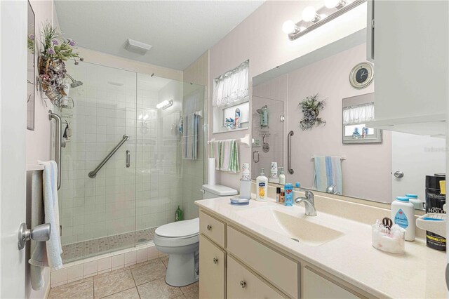 bathroom with a shower with door, vanity, toilet, and tile patterned floors