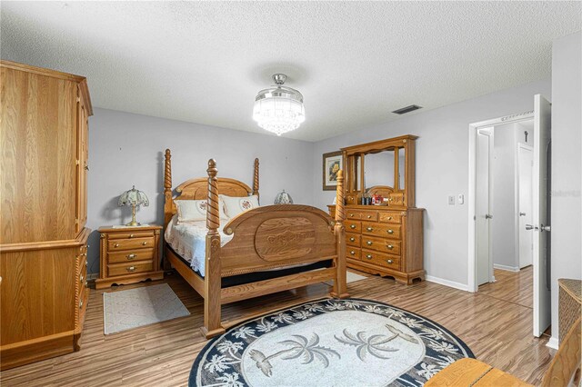 bedroom featuring light wood-type flooring, a chandelier, and a textured ceiling