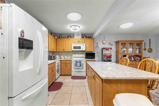 kitchen featuring white appliances, a kitchen island, light tile patterned flooring, and a textured ceiling