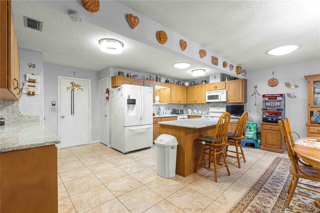 kitchen with white appliances, a textured ceiling, backsplash, a kitchen island, and a breakfast bar area