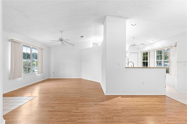 unfurnished living room with a textured ceiling, sink, ceiling fan, and light hardwood / wood-style floors