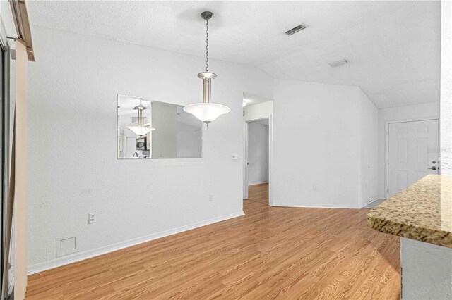 unfurnished dining area with lofted ceiling, hardwood / wood-style flooring, and a textured ceiling