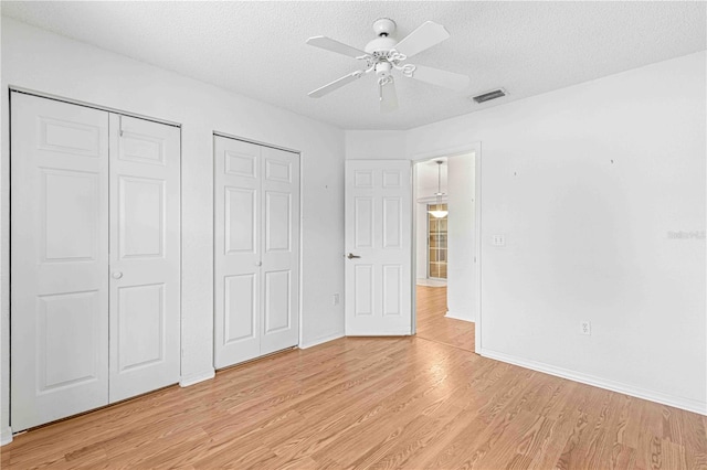 unfurnished bedroom featuring multiple closets, a textured ceiling, light hardwood / wood-style flooring, and ceiling fan