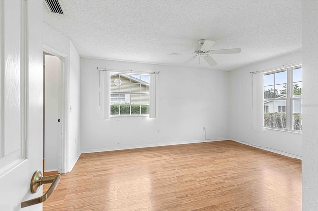 spare room with light wood-type flooring, ceiling fan, a wealth of natural light, and a textured ceiling